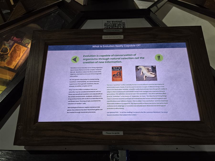 A touchscreen kiosk set into a wooden console, showing the exhibit page for What Is Evolution Really Capable Of.