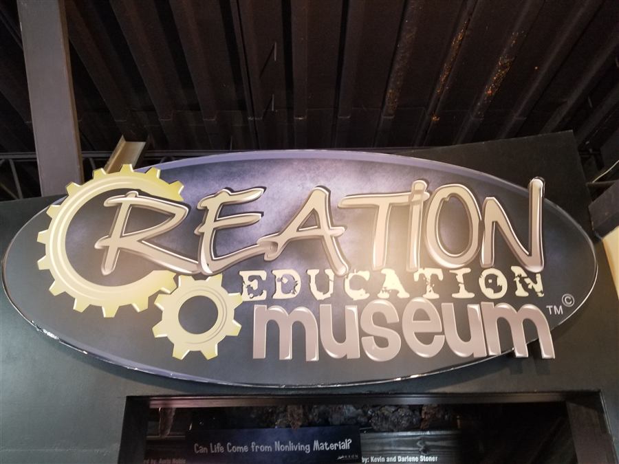 The Creation Education Museum sign, a large oval with raised metal lettering and gears, mounted above the museum doorway.