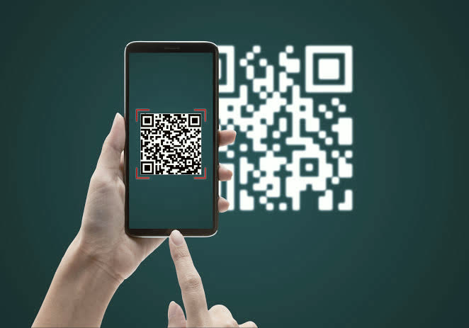 A phone held up to a QR code, with the code framed on the screen ready to scan.
