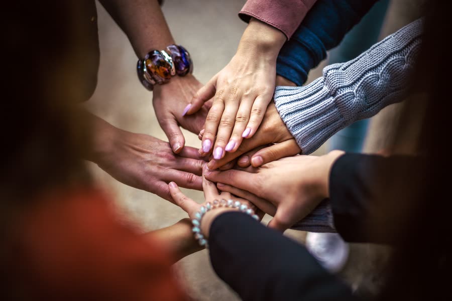 Several hands stacked one on top of another in the middle of a circle of people.