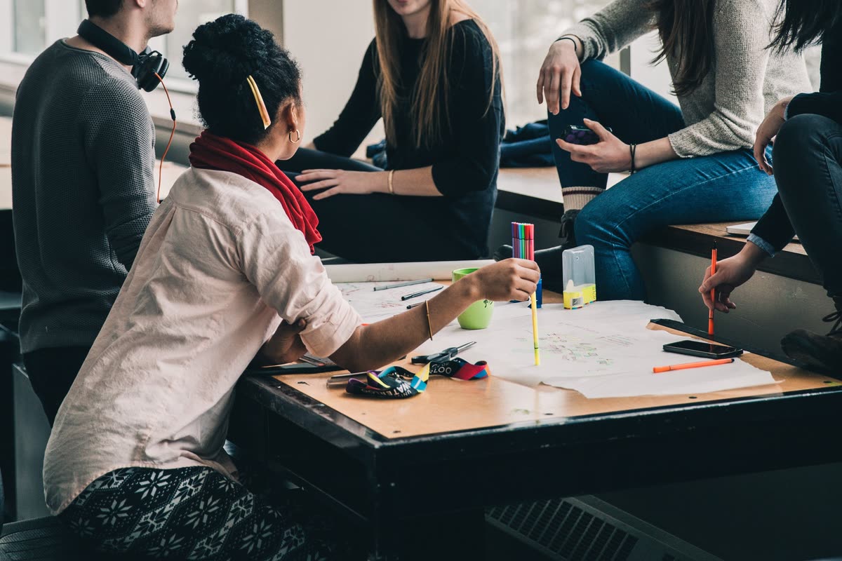 A group around a table, sketching ideas onto a large sheet of paper with coloured markers.